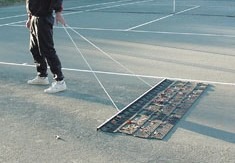 A person pulls a drag mat across a tennis court, used for maintaining surface cleanliness and leveling, essential for optimal playing conditions.