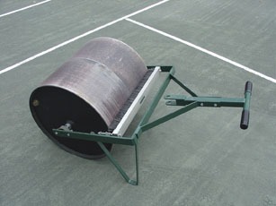 A tennis court roller, featuring a large cylindrical weight and a metal frame with a handle, used for smoothing the court surface.