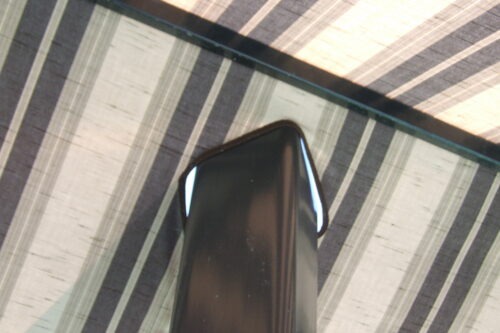 A close-up of a sleek, black electronic device resting on a striped tabletop. The image highlights the device's angular design and glossy finish.