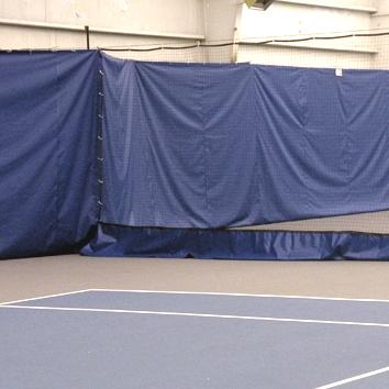 Indoor tennis court featuring a blue curtain along one side, creating a confined practice area and enhancing focus during training sessions.