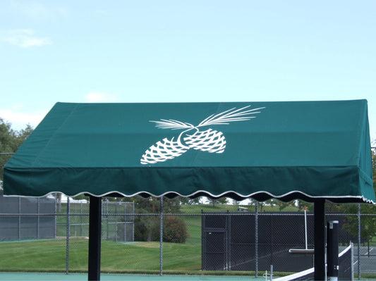 Green awning with a white pineapple design, set against a background of tennis courts. Emphasizes a tropical theme for a recreational area.