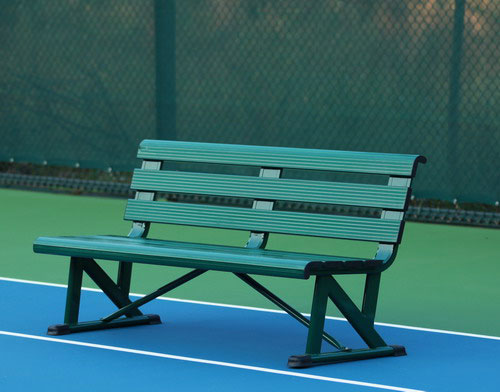 Green bench on a tennis court, set against a backdrop of a chain-link fence. Serves as a resting spot for players during matches.