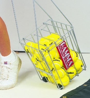 A wheeled metal basket filled with bright yellow tennis balls, with a visible GAMMA logo, is being carried beside a person's white sneaker.