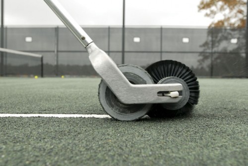 Tennis court maintenance tool with a brush attachment rolls along a freshly marked line on a green hard court, ensuring proper playing conditions.