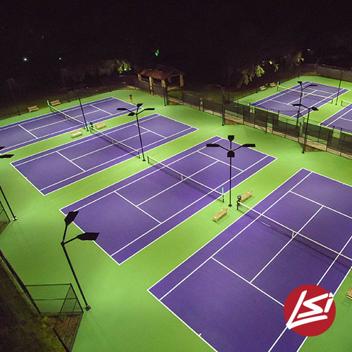 Illuminated tennis courts featuring vibrant purple surfaces and green surroundings at night, highlighting a recreational sports facility.