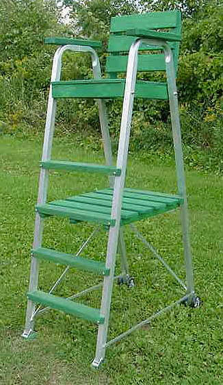 Tall green lifeguard chair with a wooden seat and metal frame, positioned on grass, used for overseeing pool activities.