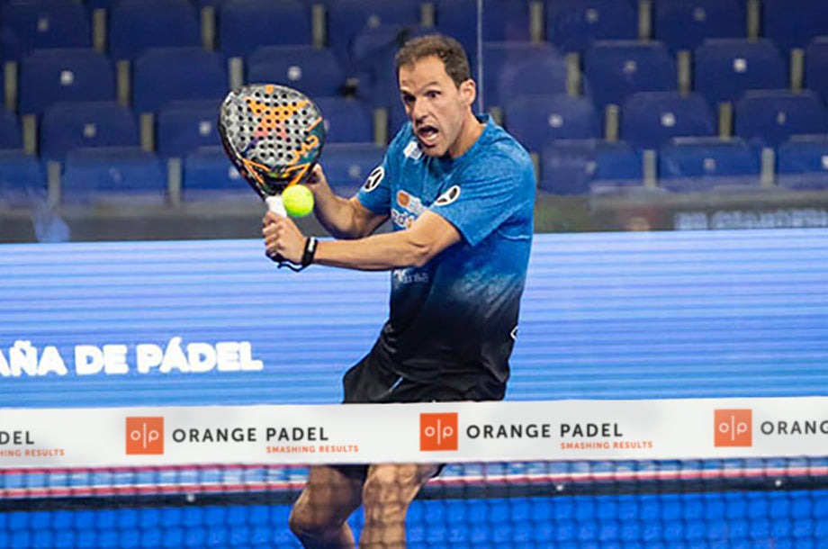 A player in a blue sports shirt swings a padel racket to hit a yellow ball during a match, showcasing the excitement of competitive padel.