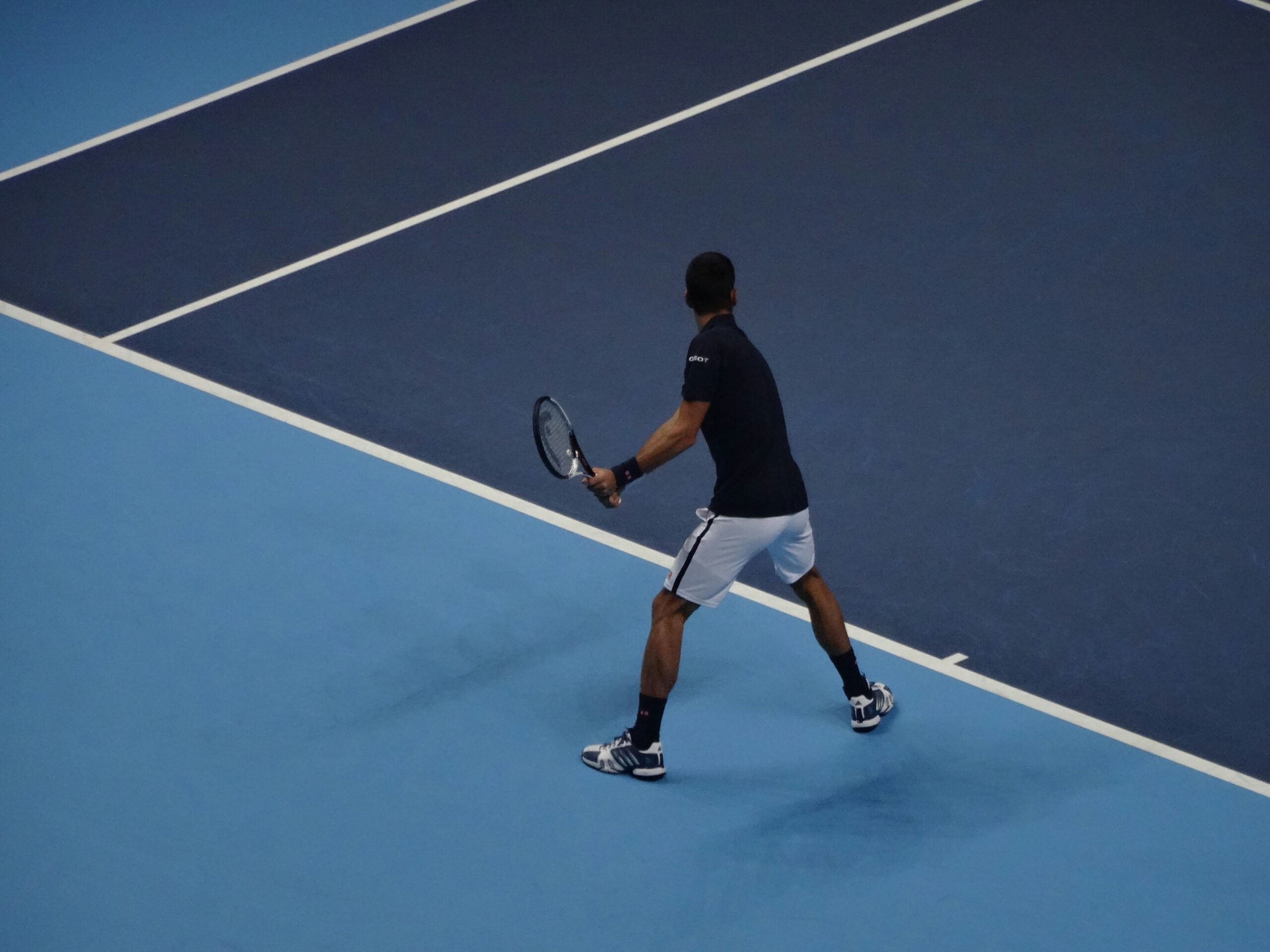 A tennis player prepares to serve on a blue court, demonstrating focus and athleticism in a competitive match setting.