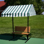 Wooden bench with a green and white striped canopy in a grassy park setting, providing shade for relaxation. Ideal for outdoor seating areas.