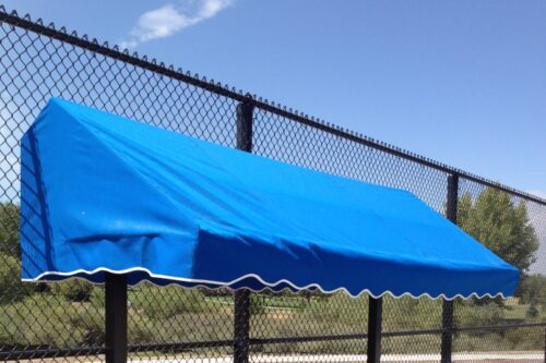 Bright blue awning with a scalloped edge, mounted on a fence, providing shade in an outdoor setting. Ideal for relaxing or social gatherings.