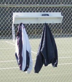 Two jackets, one white and one navy, hanging on hooks attached to a white shelf on a chain-link fence at a tennis court.