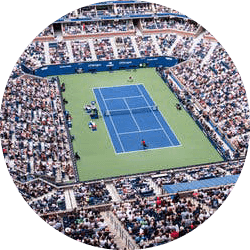 Aerial view of a packed tennis stadium during a match, showcasing players on a blue court surrounded by enthusiastic spectators.