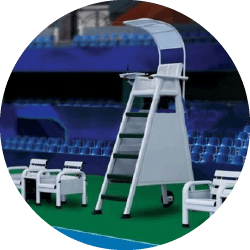 Lifeguard chair on a pool deck, surrounded by empty lounge chairs and blue seating, indicating a recreational or competitive swimming setting.