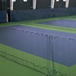 Indoor tennis courts feature multiple playing areas separated by nets. The green court surfaces contrast with blue barriers, creating a structured training environment.