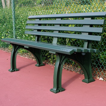 Green metal bench on a red court surface, bordered by a chain-link fence. Ideal for resting in an outdoor recreational area.