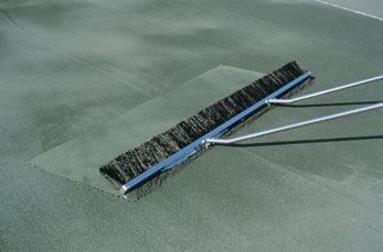 A squeegee with a long handle is shown smoothing out a green surface, likely a court or flooring material, for a professional finish.