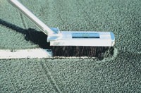 A close-up of a cleaning tool brushing debris off a green tennis court surface near a white line, illustrating maintenance practices for sports facilities.